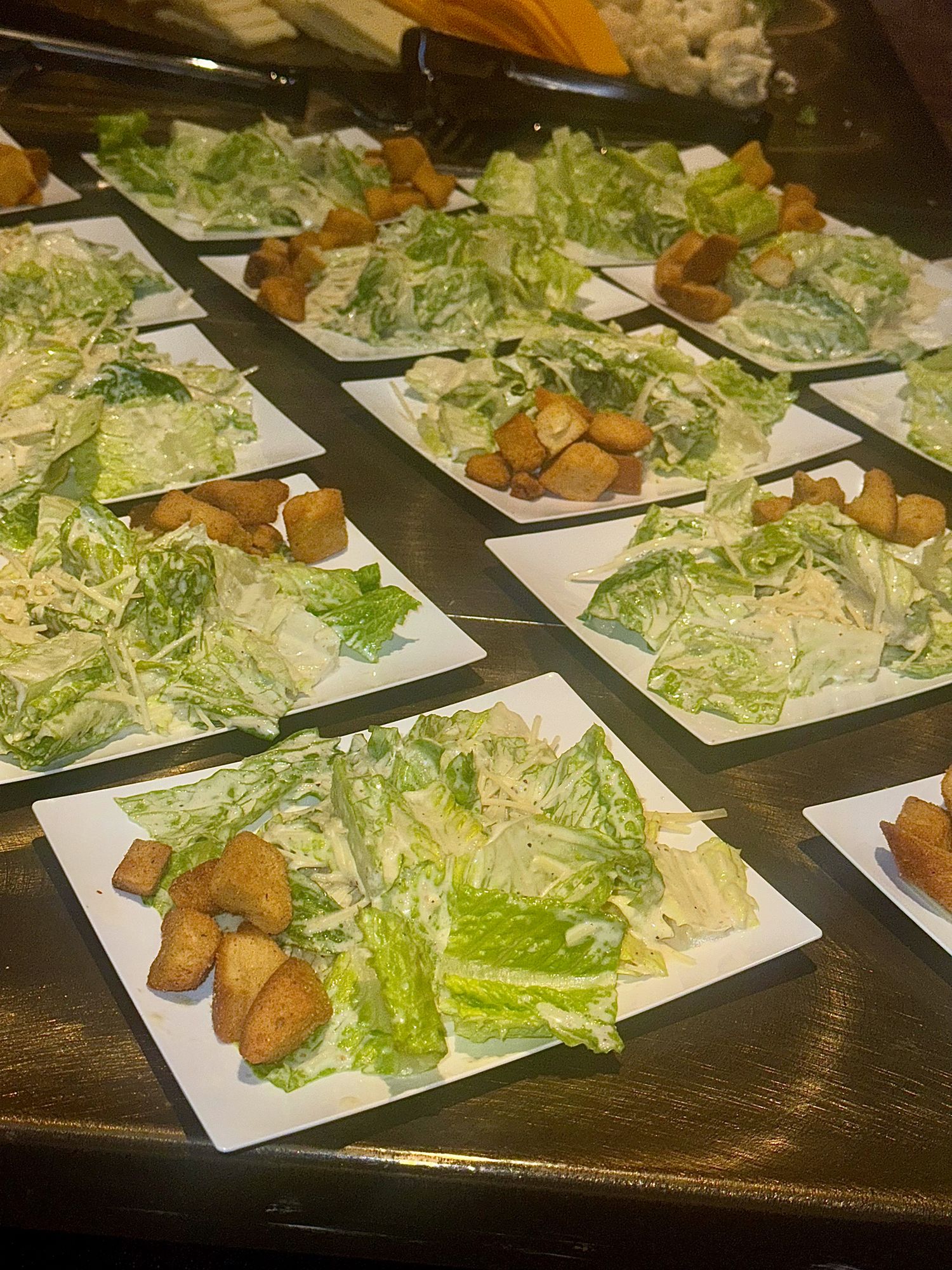 Multiple plated salads with crisp lettuce and fried appetizers arranged in neat rows on a dark surface.