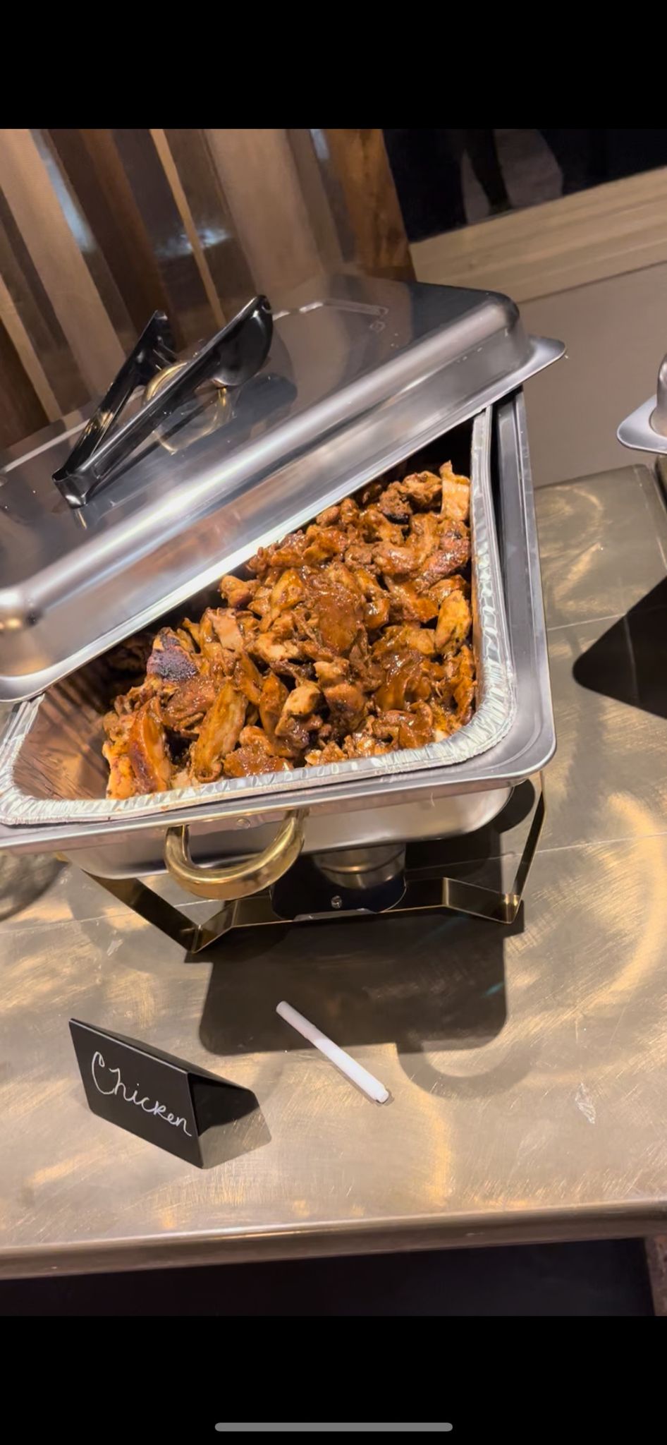 Catering trays filled with seasoned chicken or meat at a buffet setup.