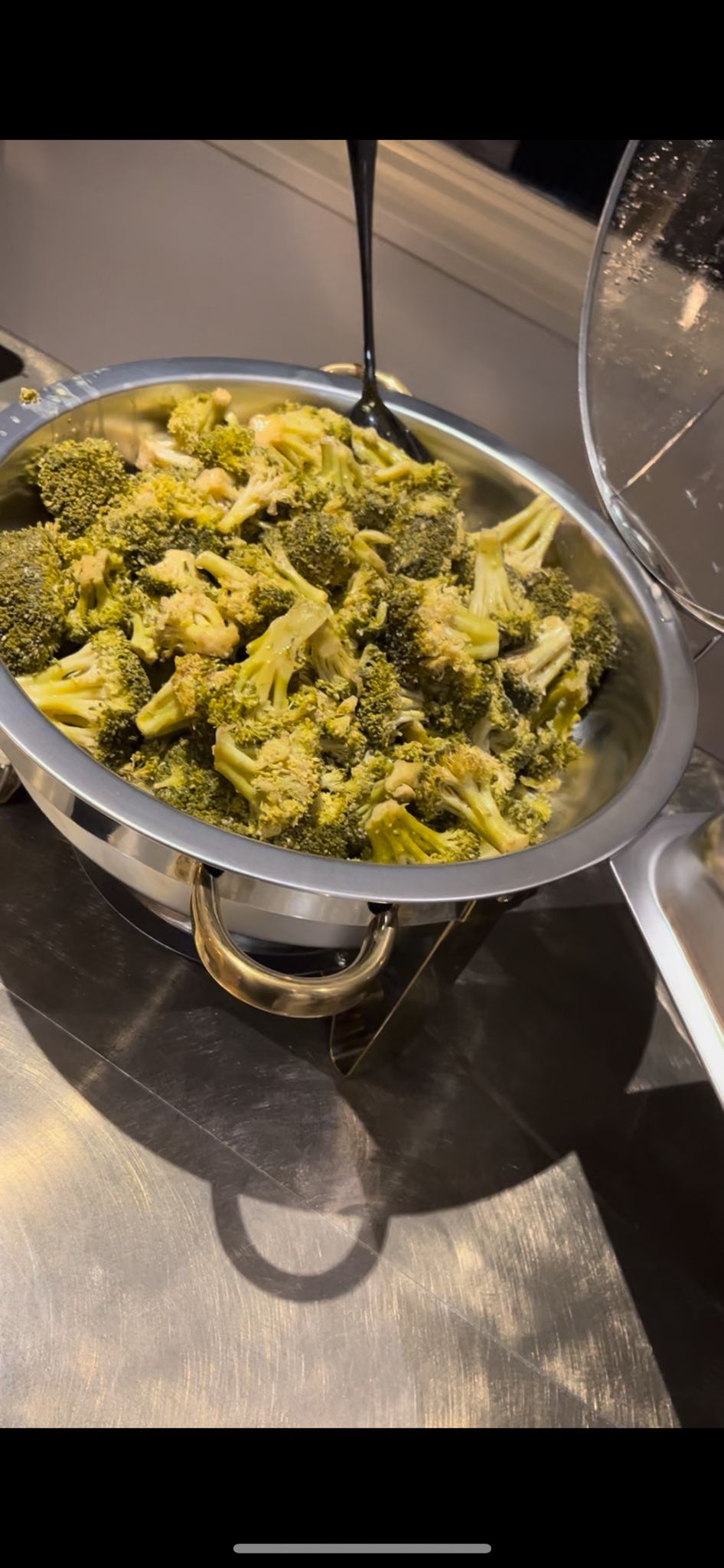 Steamed broccoli florets served in a metal pan on a dark surface.