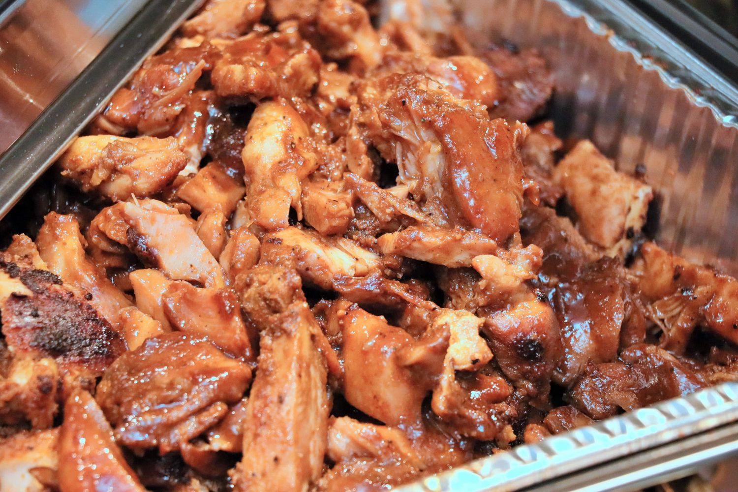 Glazed BBQ chicken pieces in a catering tray with rich brown sauce.