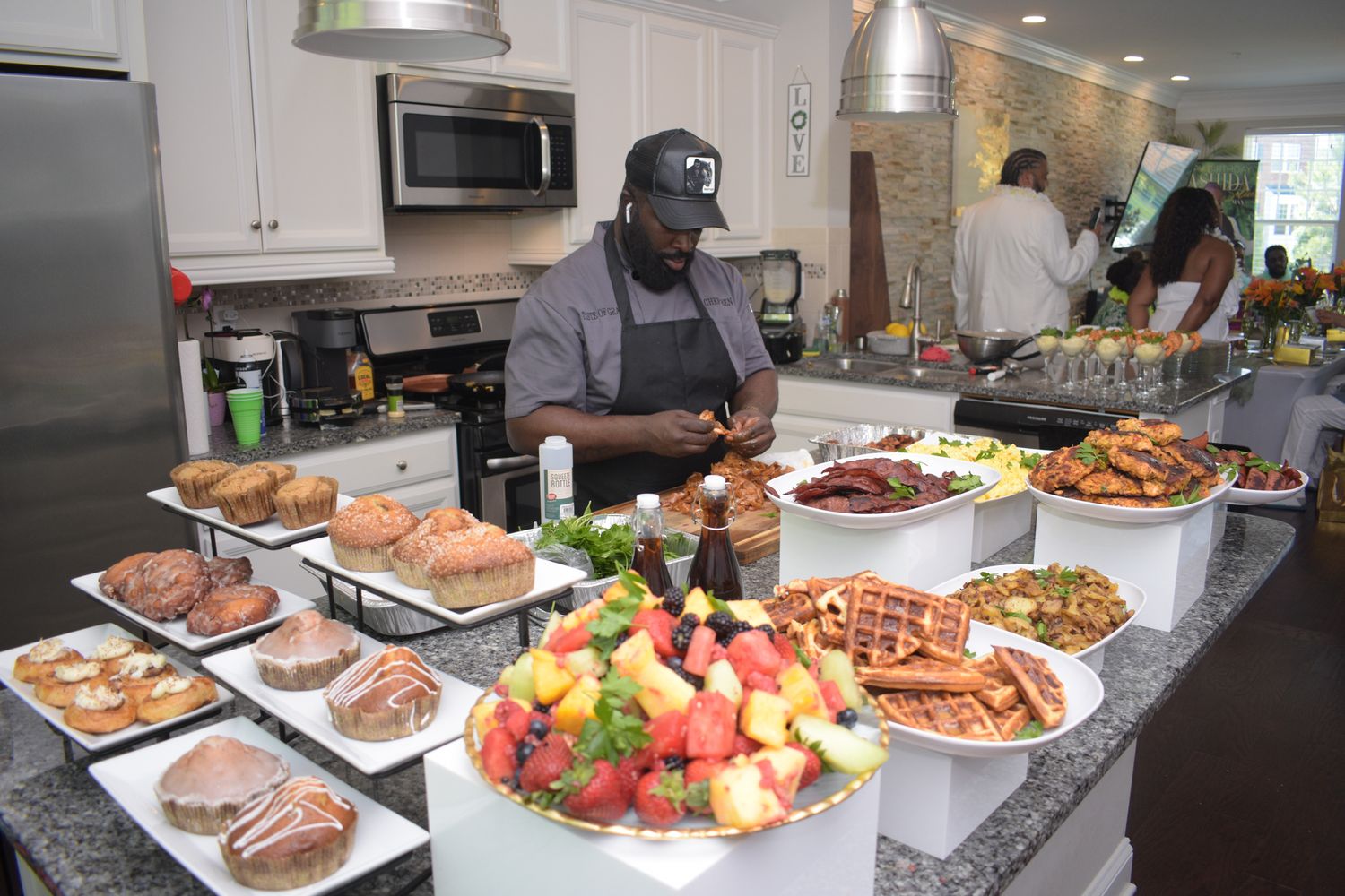 Catering buffet spread with various dishes, fruits, and prepared foods on white serving platters.