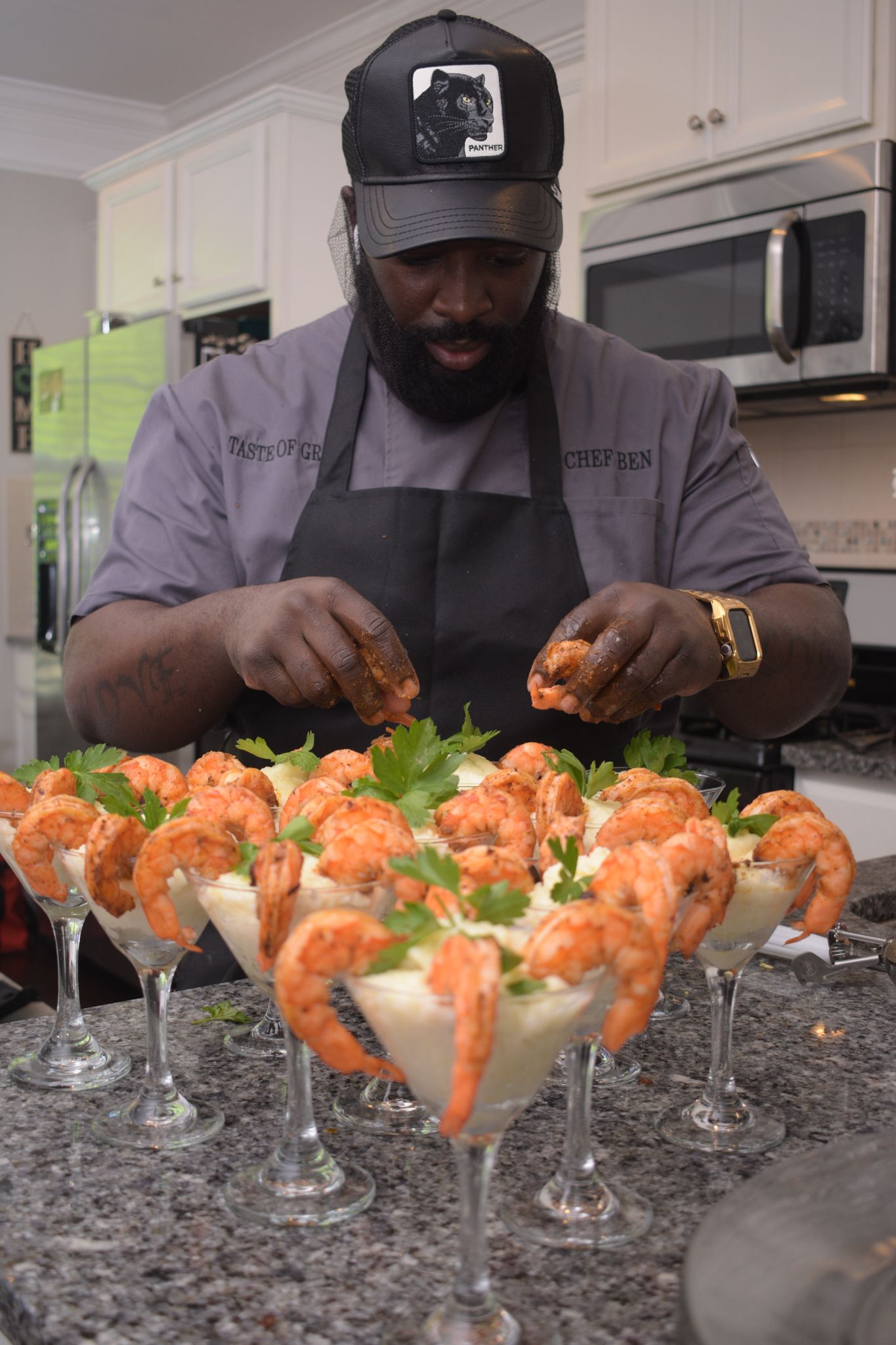 Shrimp cocktails being arranged in martini glasses on granite countertop.