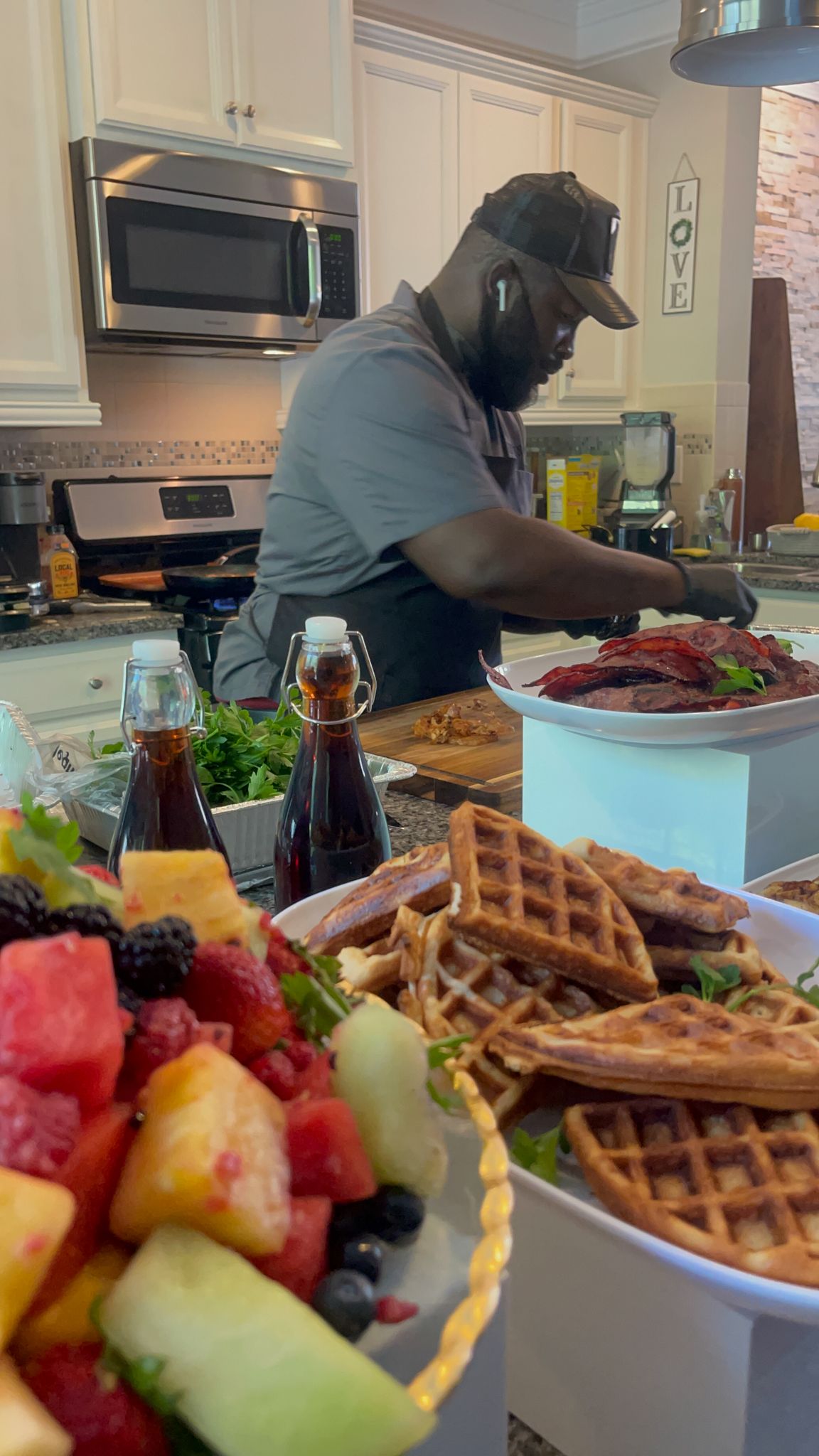 Fresh waffles served with colorful mixed fruit including watermelon, pineapple and berries on white plates in a modern kitchen.