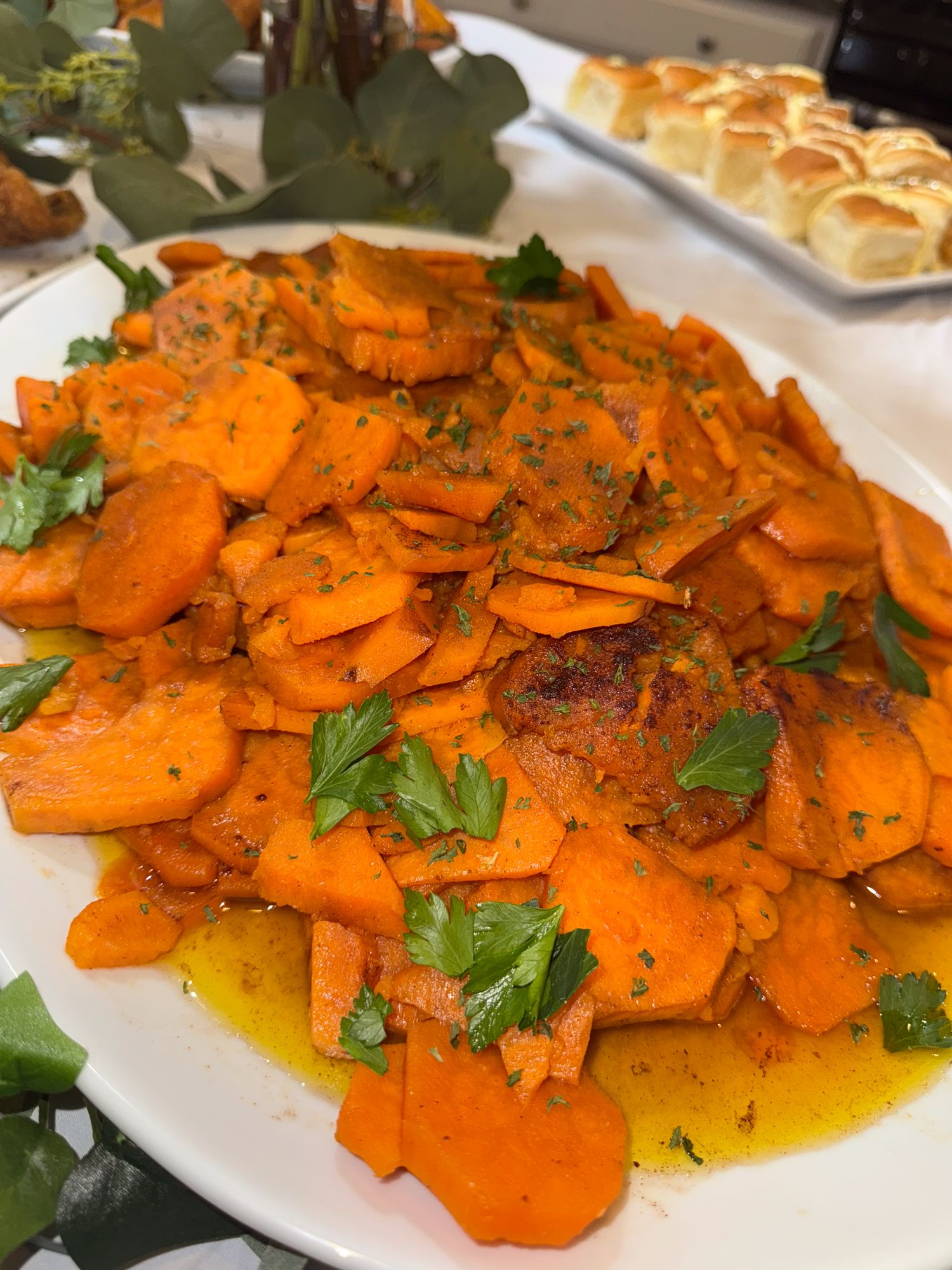 Roasted carrots garnished with fresh herbs and spices served on a white platter in vibrant orange hues.