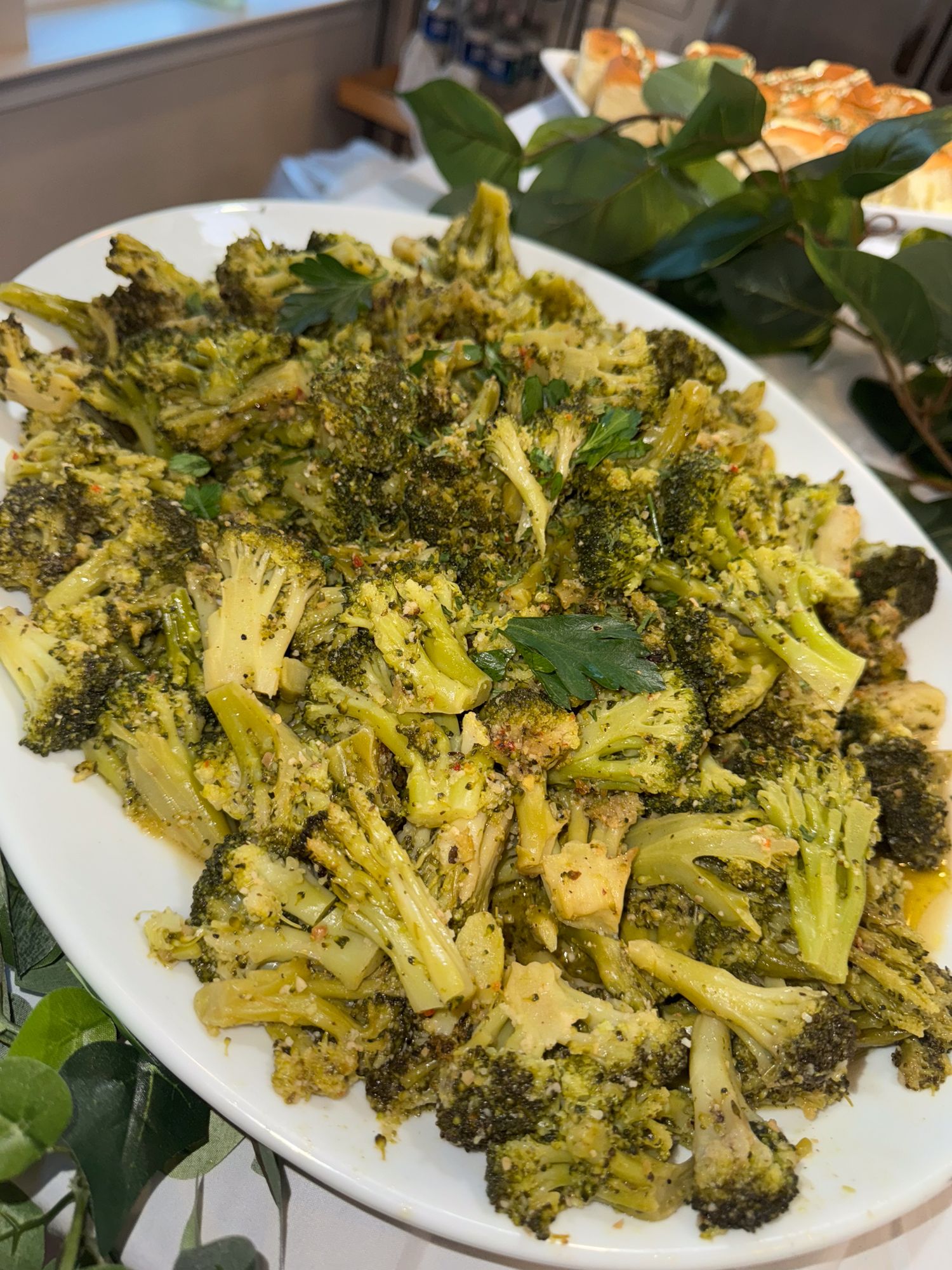 Roasted broccoli florets seasoned and served on a white platter with fresh herbs.