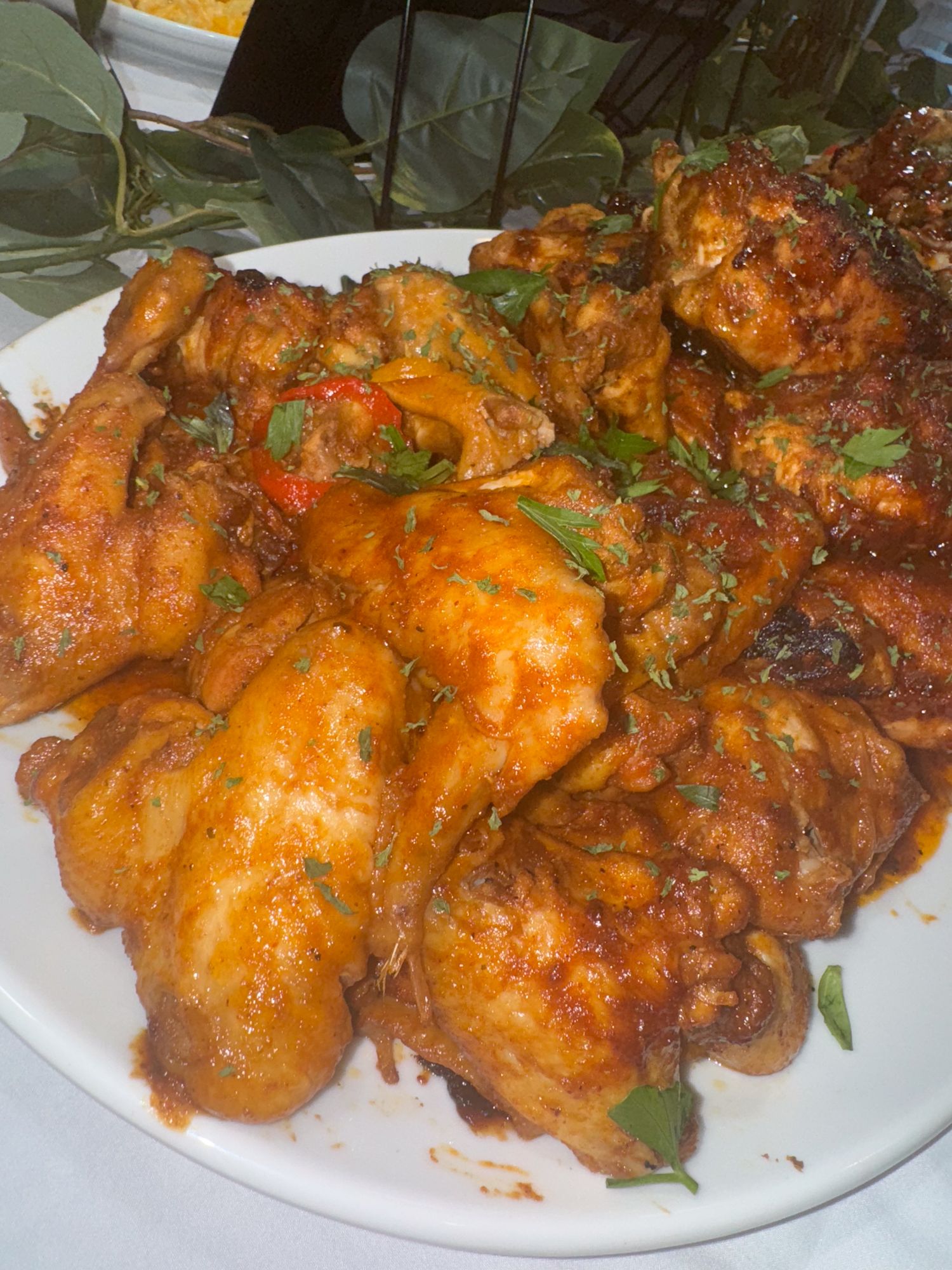 Spicy glazed chicken wings garnished with fresh herbs on a white plate.