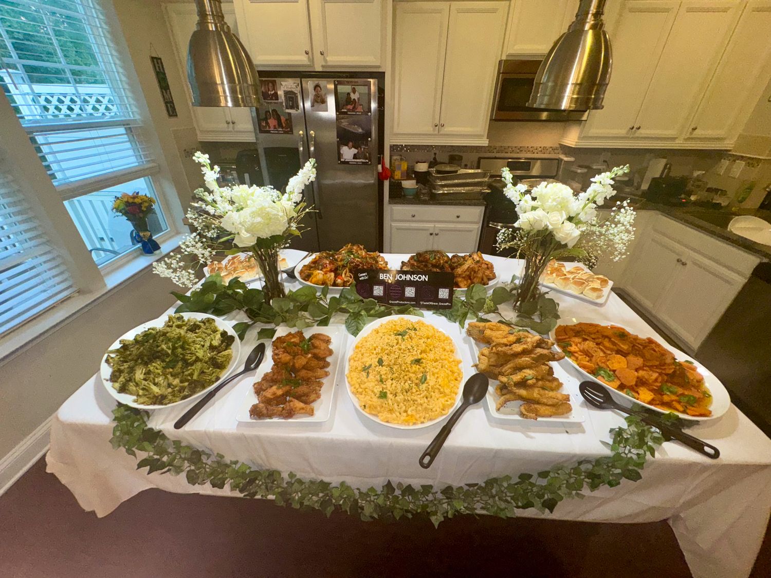 Long buffet table decorated with greenery garland displaying various appetizers and party dishes.