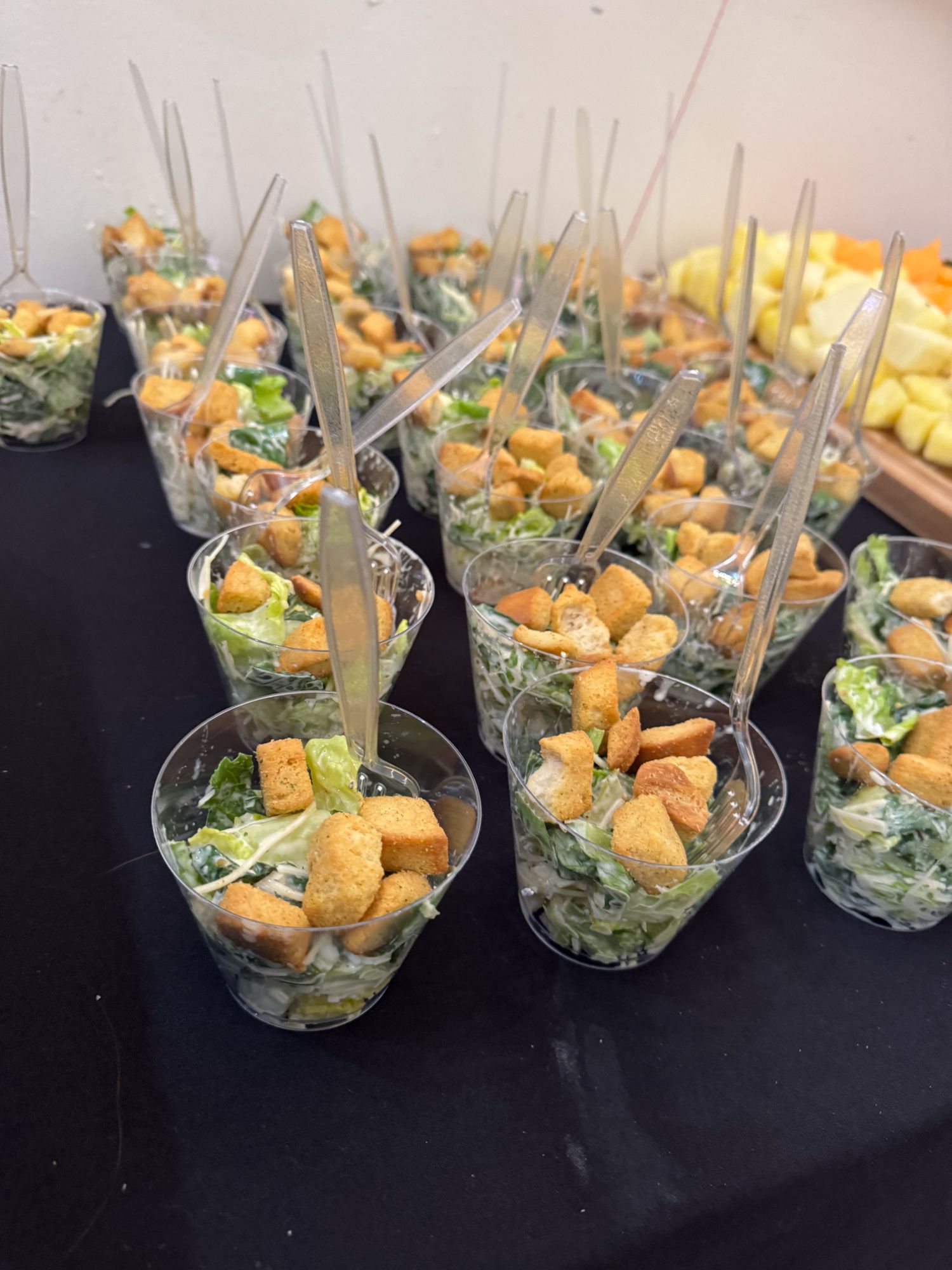 Individual serving cups of Caesar salad with croutons arranged on a black tablecloth.