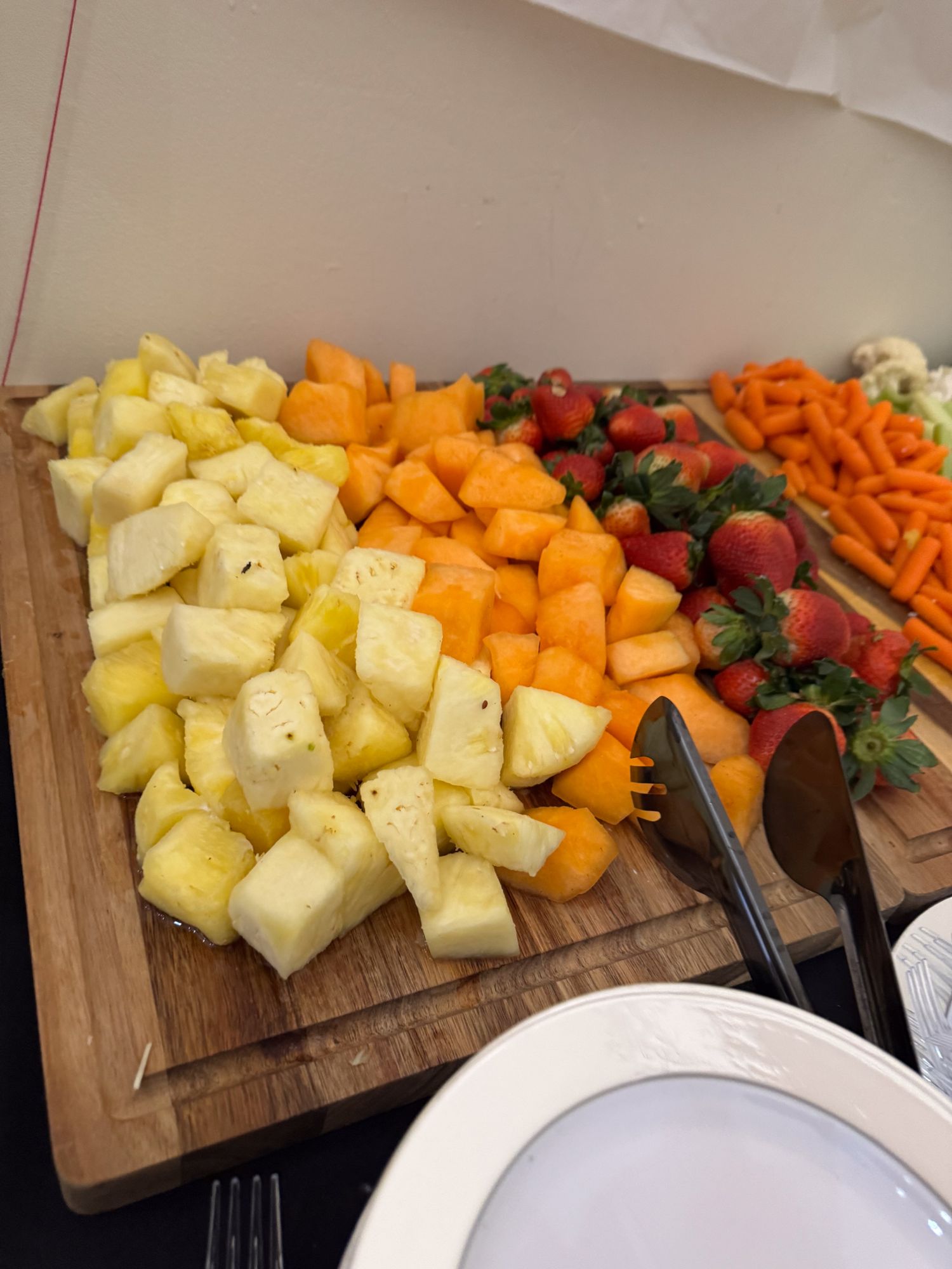 Fresh cut fruit and vegetables arranged on a wooden cutting board including pineapple, carrots, and strawberries.