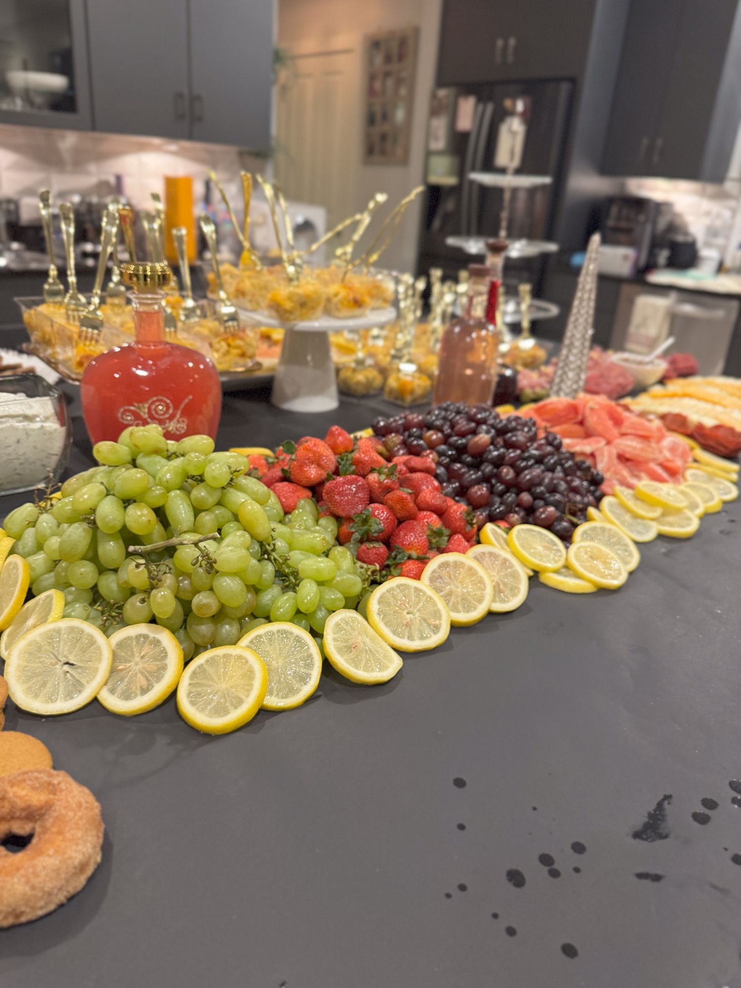 Fresh fruit platter with sliced lemons, grapes, strawberries and cherries arranged on a dark counter.