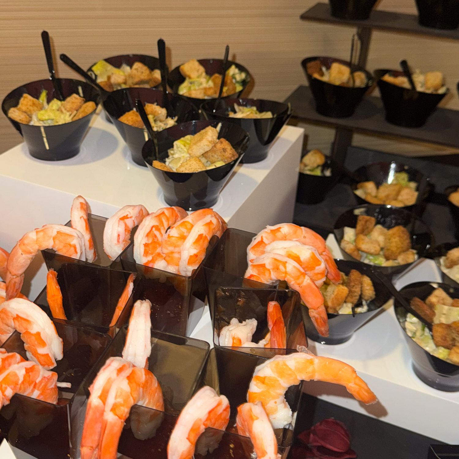 Multiple plates of appetizers featuring large shrimp cocktails arranged in rows on a buffet table.