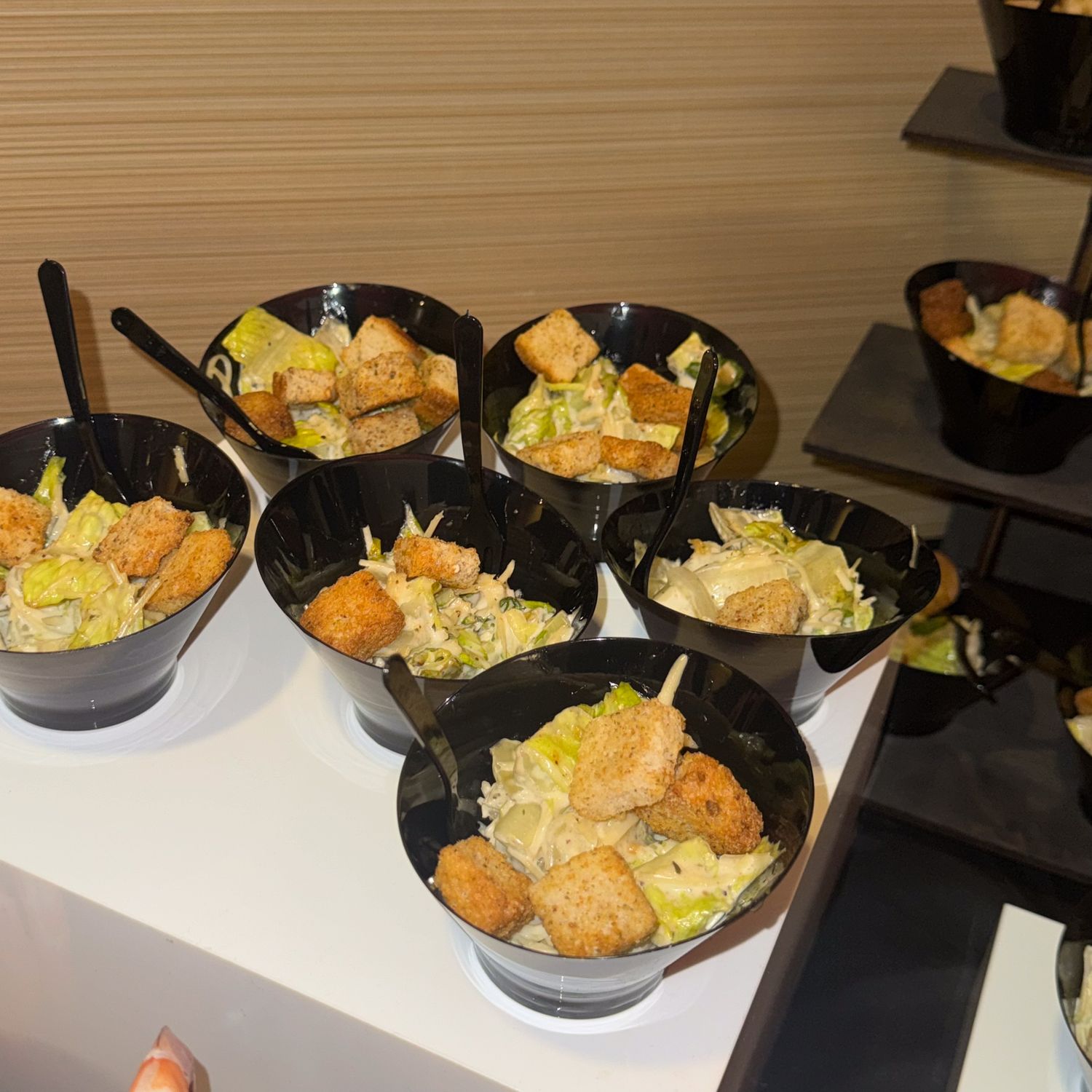 Black serving bowls filled with pasta or rice dishes arranged in a row on a buffet table.