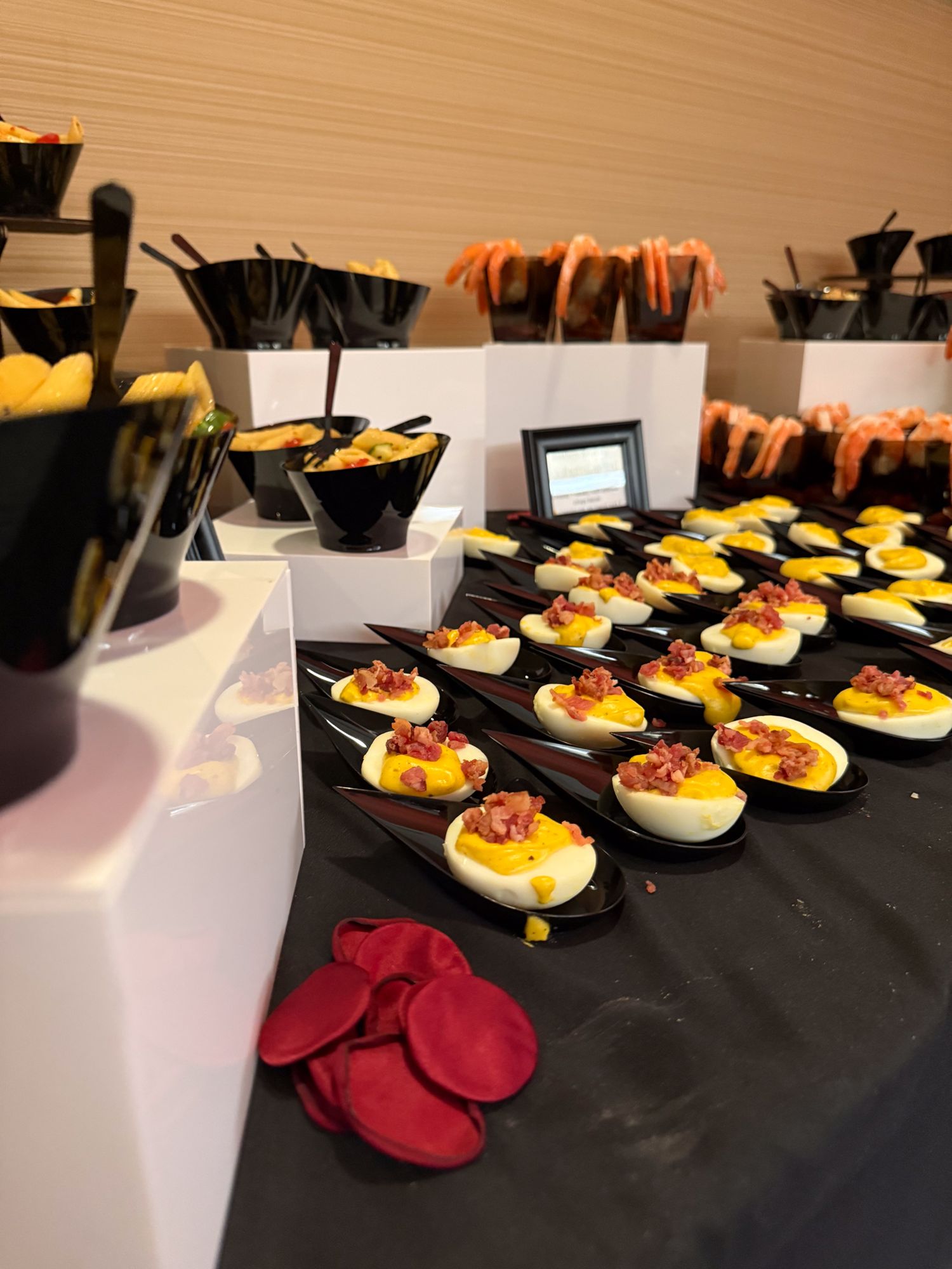 Rows of deviled eggs garnished with red toppings are elegantly displayed on black serving platters at a catered event.