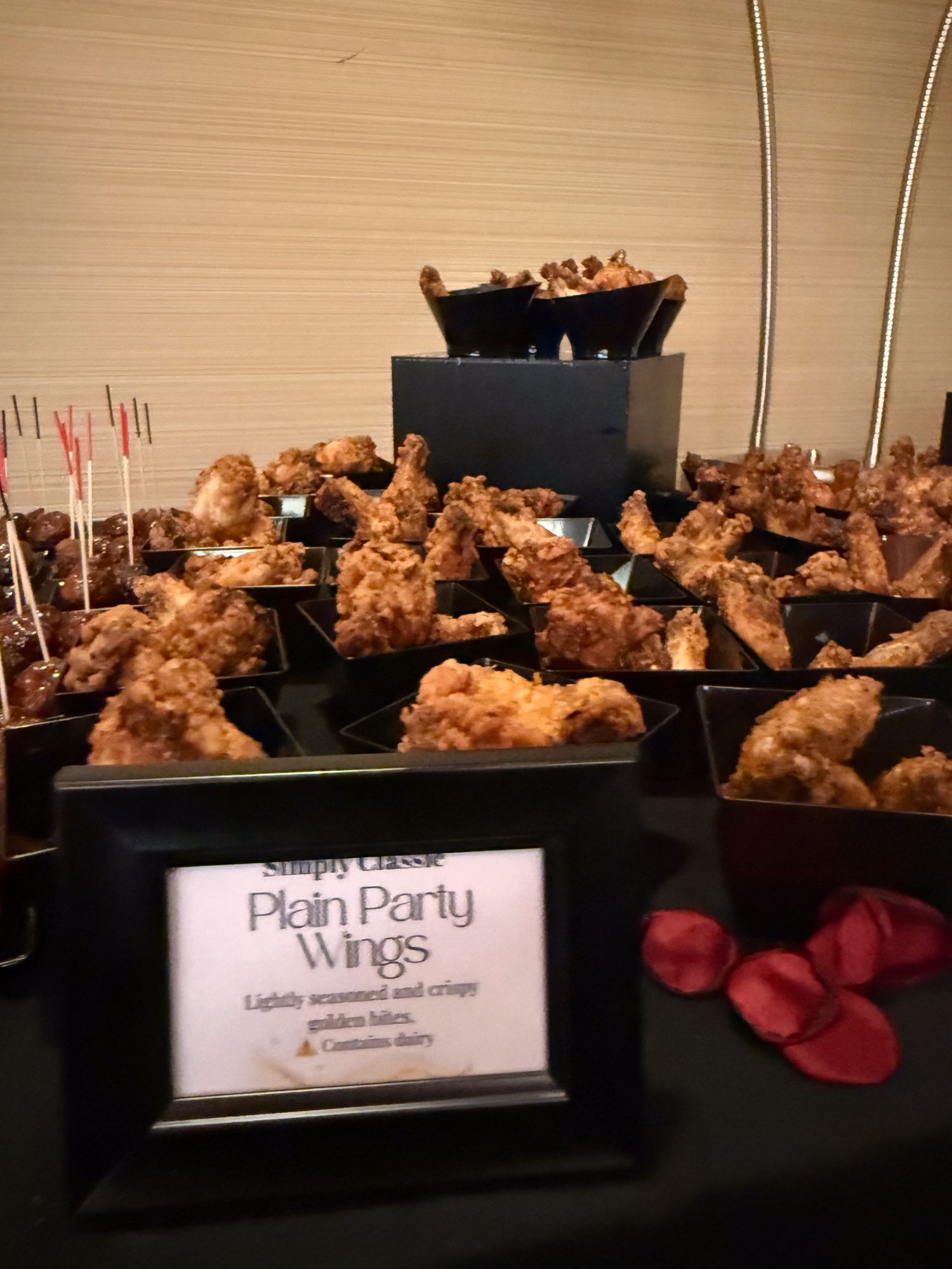 Rows of golden-brown chicken wings arranged on black serving platters with a labeled display sign at a catered event.