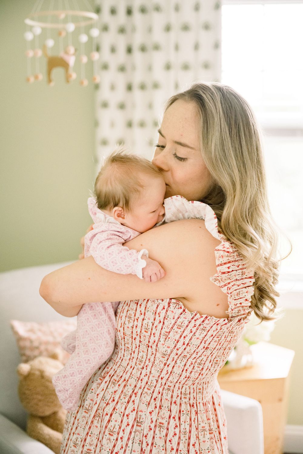 A tender moment captured in warm sunlight as a baby rests on a shoulder wearing a smocked floral dress.
