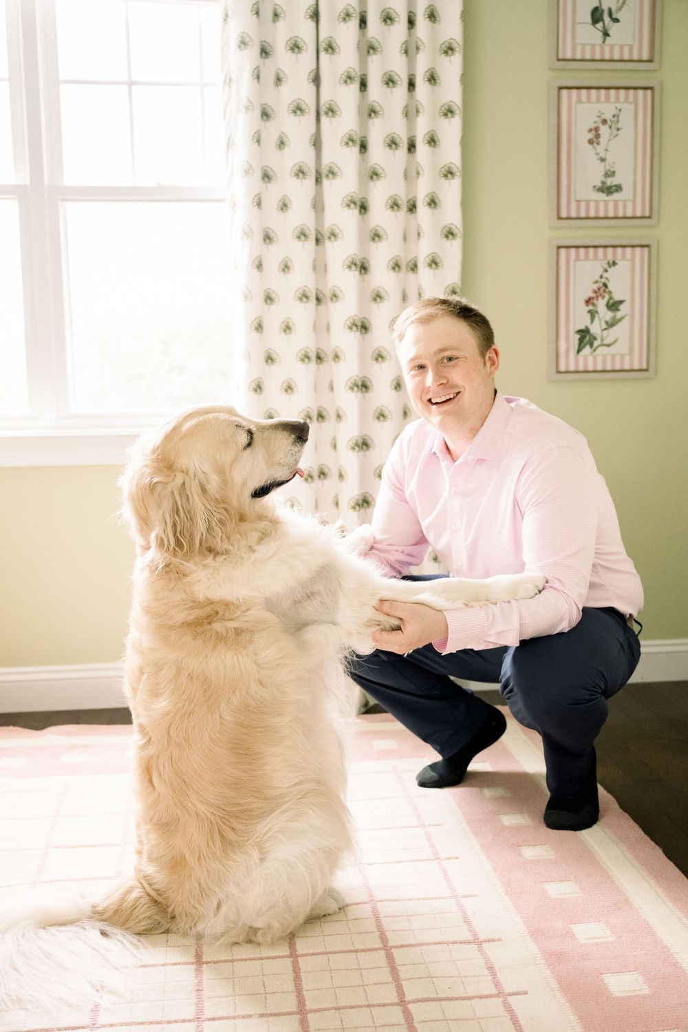 A golden retriever sits on a pink and white checkered rug while interacting with someone in a pink shirt.