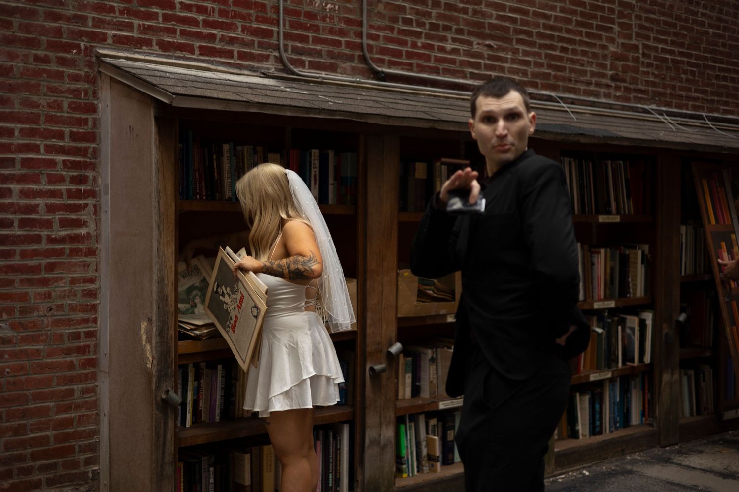 A couple stands in front of a bookshelf-lined wall in what appears to be a library or bookstore.