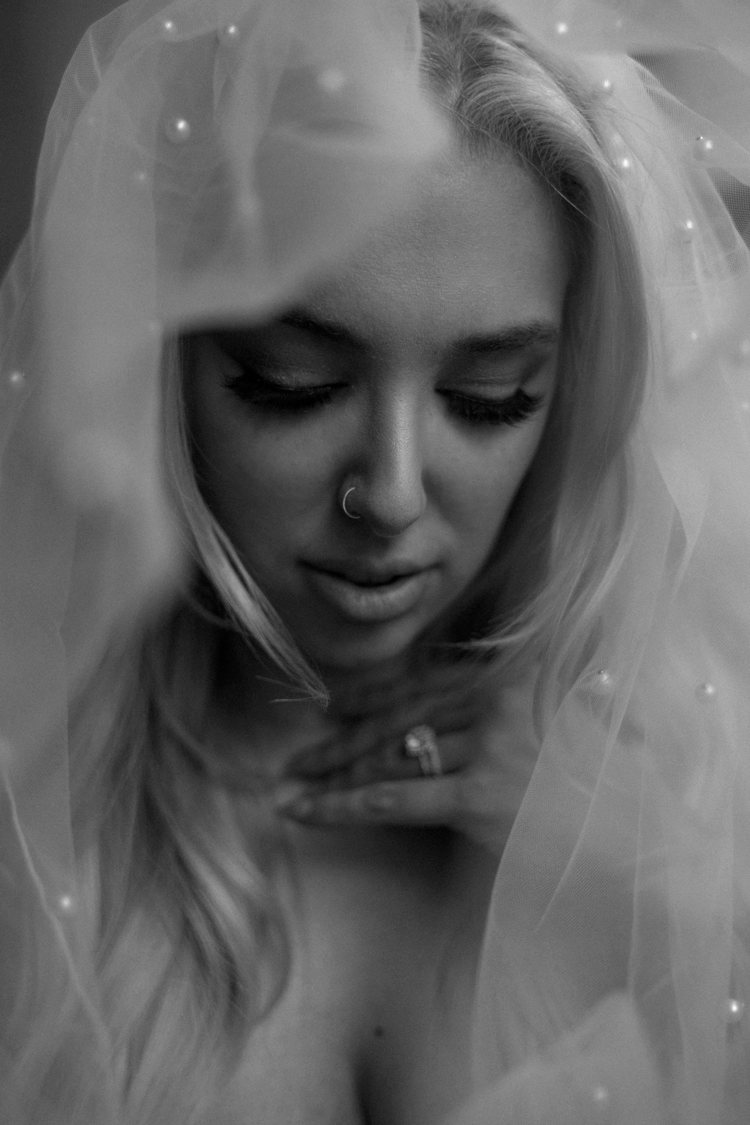 A series of soft black and white portraits showing a person with blonde hair and a nose piercing looking downward.