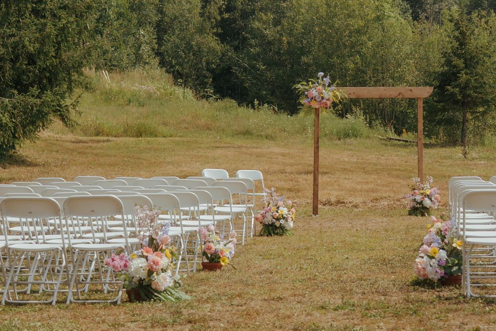White folding chairs arranged in rows on a grassy hillside for an outdoor wedding ceremony with floral decorations.