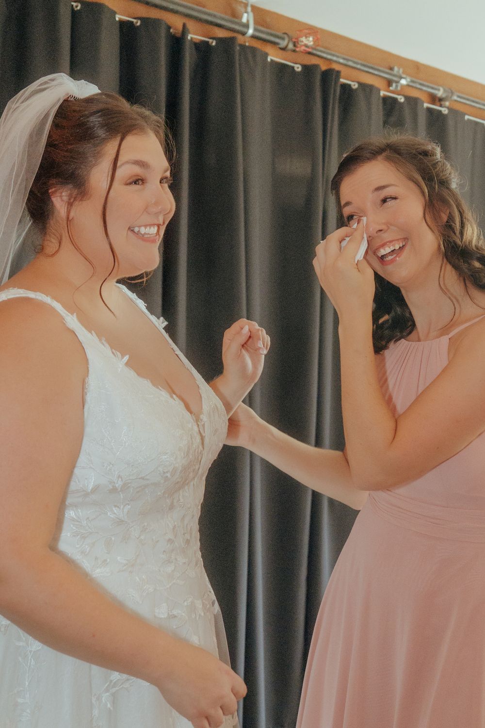 Joyful moments shared between a bride in white and bridesmaid in pink during wedding preparations.