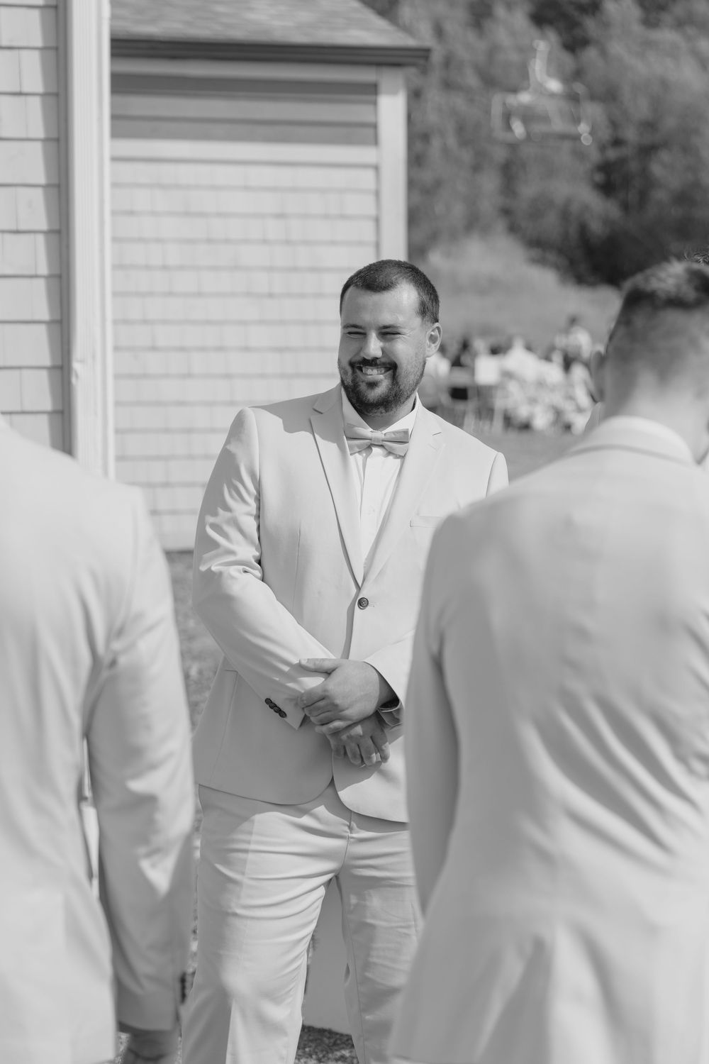 Wedding attendees in white and light colored formal attire gather outside a building.