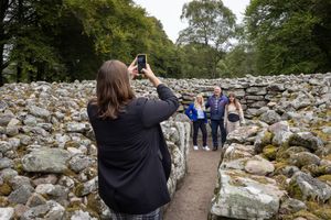 Visitors explore ancient stone ruins along a winding path through historic archaeological site in Scotland.