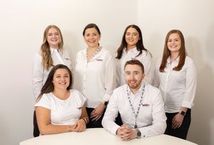 Group of healthcare professionals in white uniforms sitting and standing together in a modern office setting.