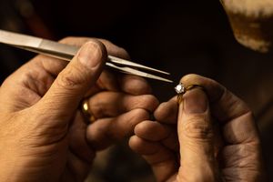 Close-up view of hands using precision tweezers to handle small components in jewelry making or repair work.