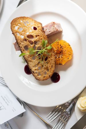 Elegant plated dish featuring sliced bread, citrus segments, and a sauce garnished with microgreens on white porcelain.