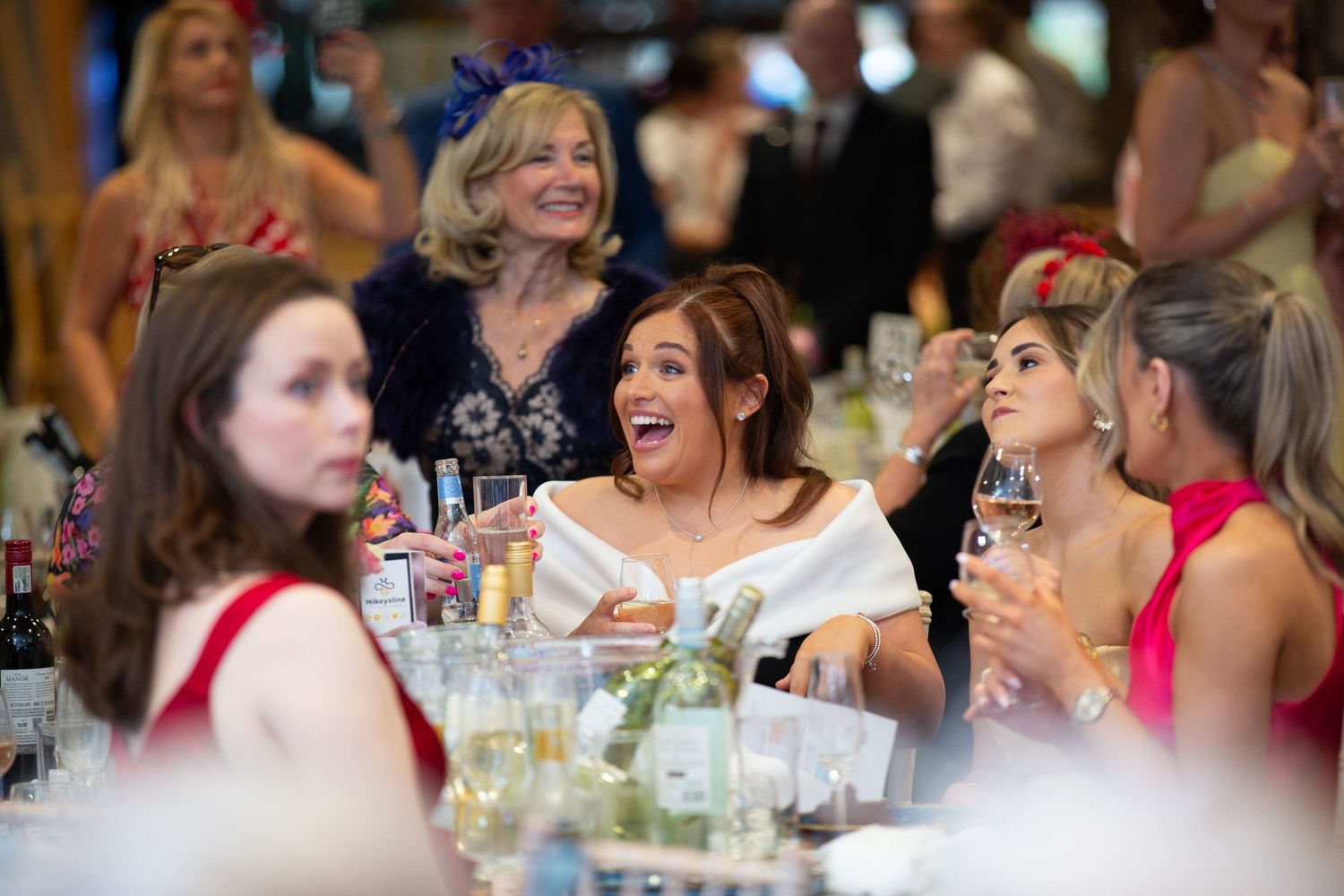 Party guests laugh and smile while enjoying drinks and conversation at a festive indoor gathering.