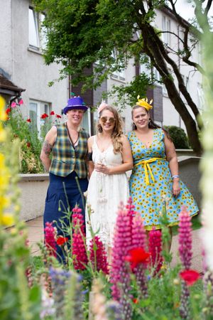 A group poses behind vibrant pink and purple lupine flowers blooming in a garden setting.
