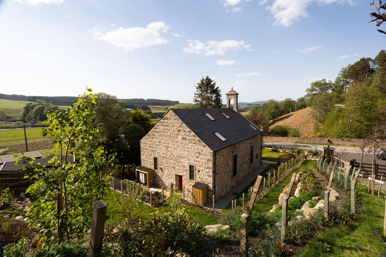 Panoramic view of rustic stone cottages nestled in rolling green countryside with blue sky and scattered clouds above.
