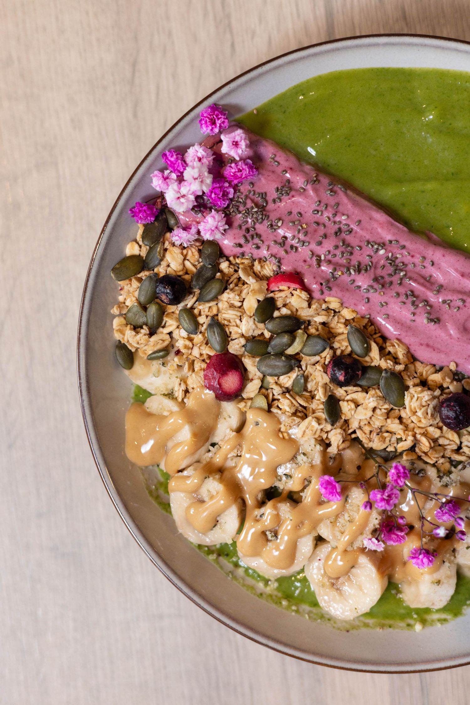 Elegant plated dish with shrimp, vibrant green sauce, granola topping and pink edible flowers on a ceramic plate.