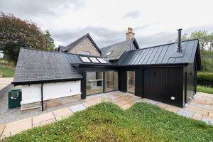 Modern black and white barn conversion with sleek metal roofing and large windows nestled in rural countryside setting.