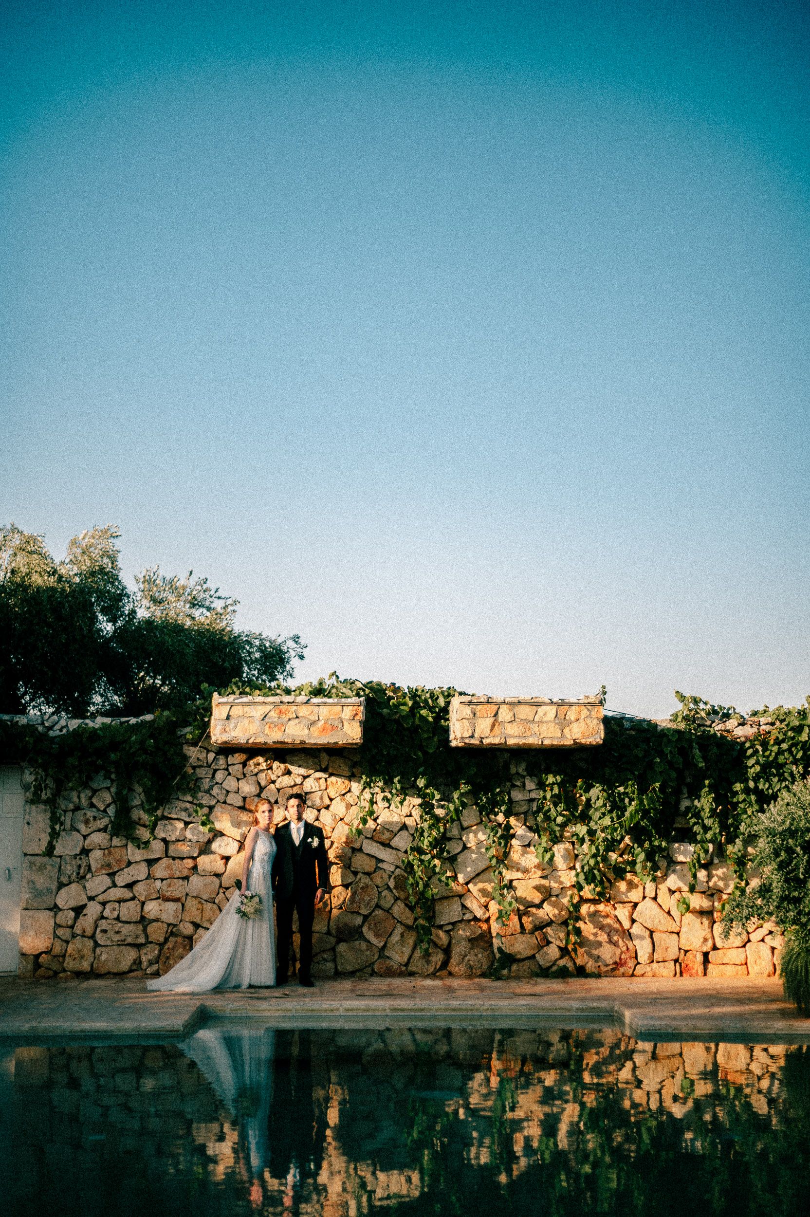 A rustic stone wall and wooden structure creates a romantic silhouette against a serene blue sky at sunset.