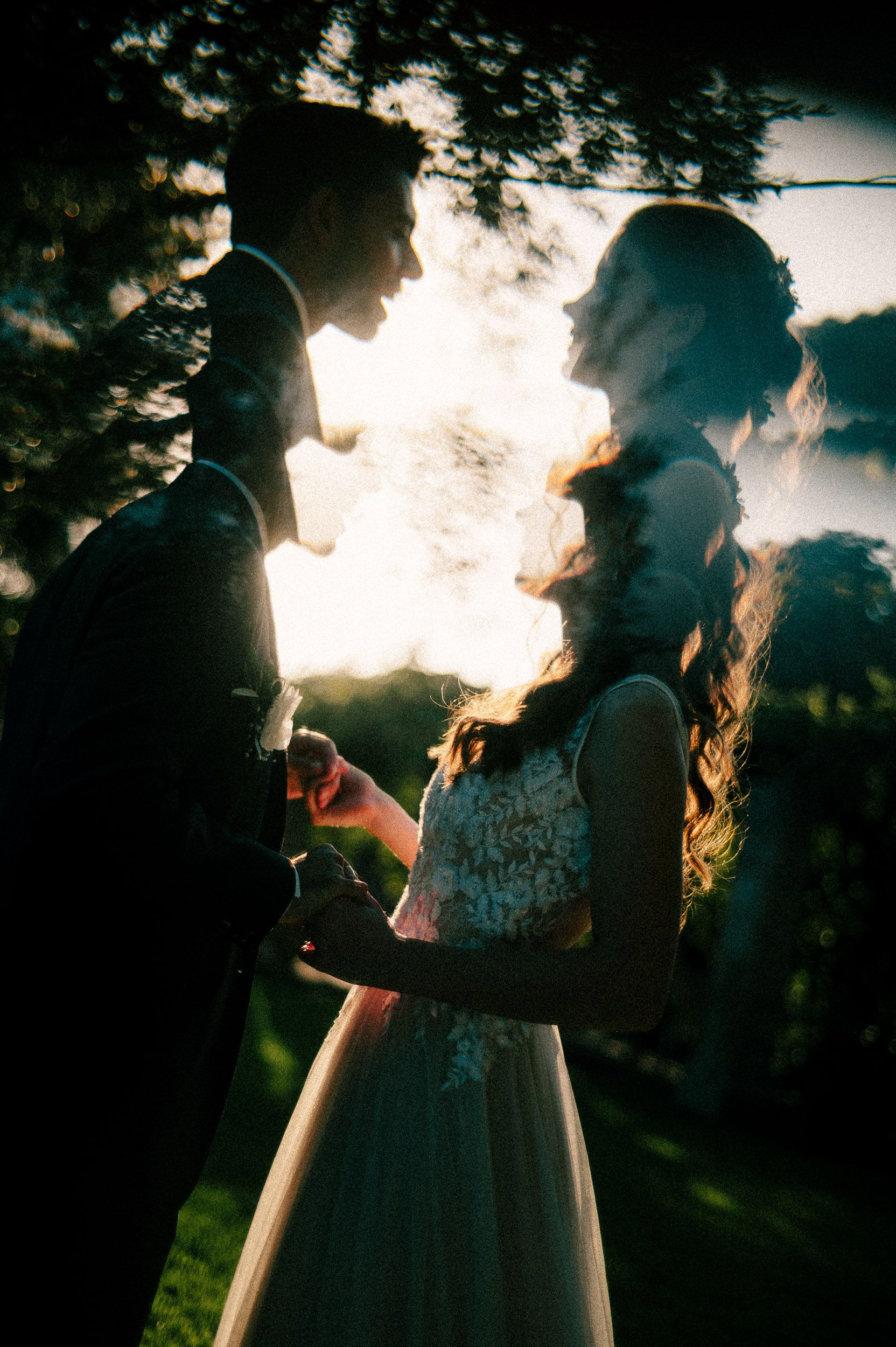 Silhouetted figures exhale vapor from electronic cigarettes against a dramatic sunset sky, creating an ethereal backlit effect.