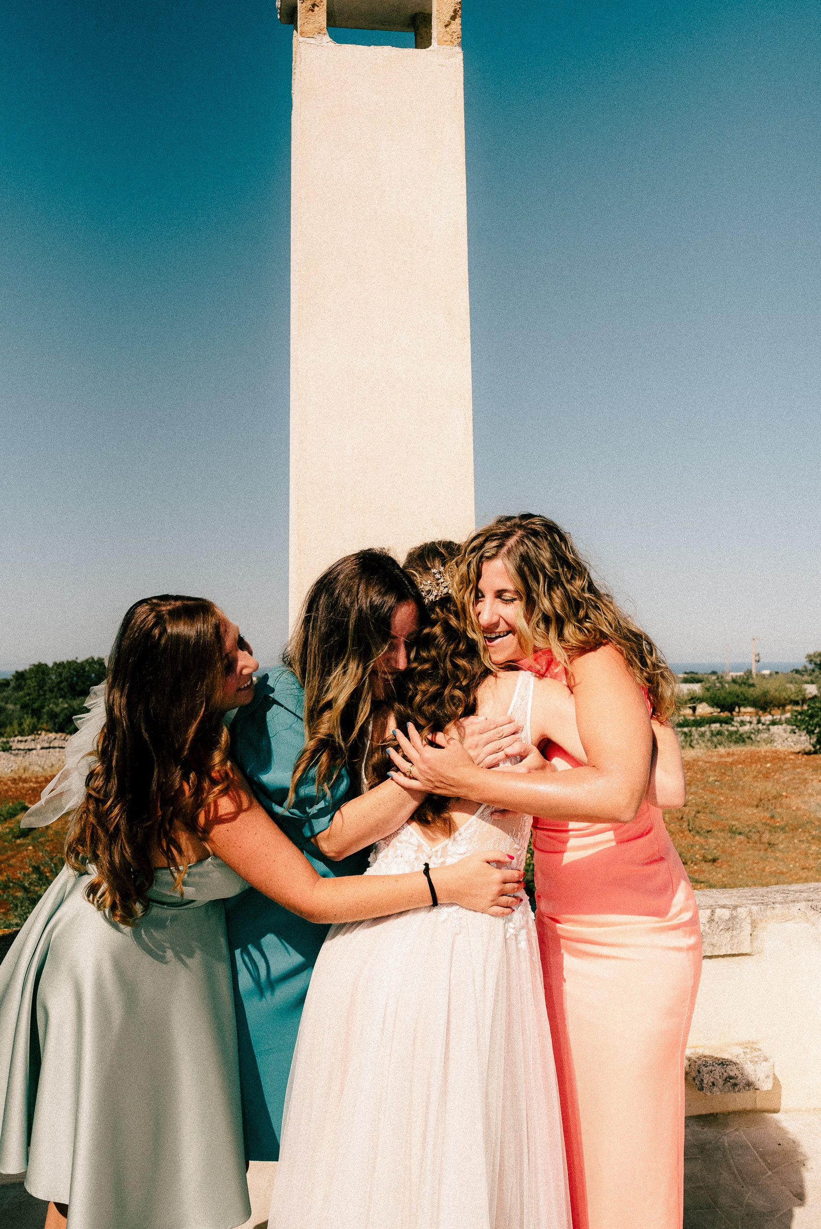 A sequence of four candid photos showing friends embracing and sharing a group hug outdoors on a sunny day.