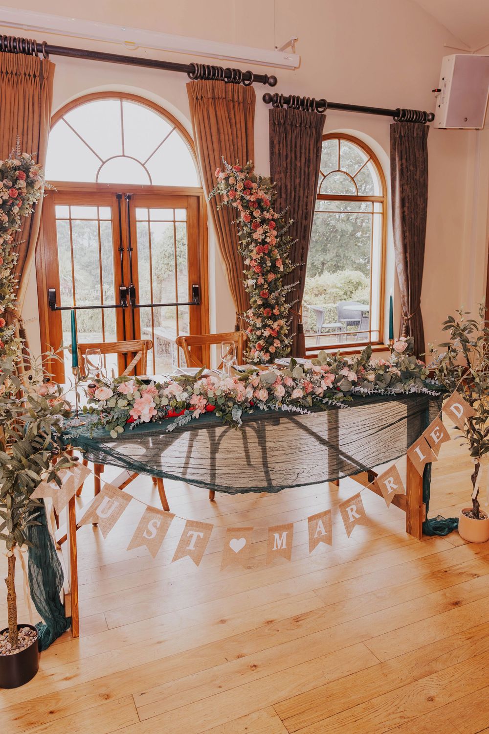 Elegant wedding venue space with arched windows, hardwood floors and floral arrangements adorned with a banner.