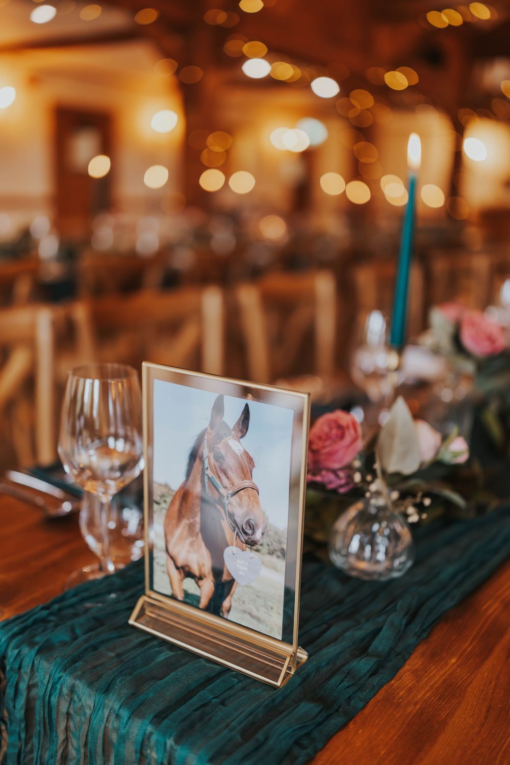 Framed photograph on wooden table with emerald green velvet runner and wine glasses in warm ambient lighting.