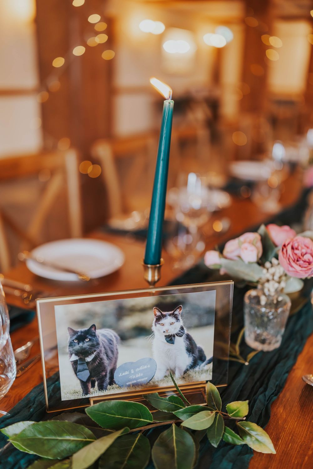 Wedding table setting with teal candle and framed photo of two cats alongside pink roses and greenery.