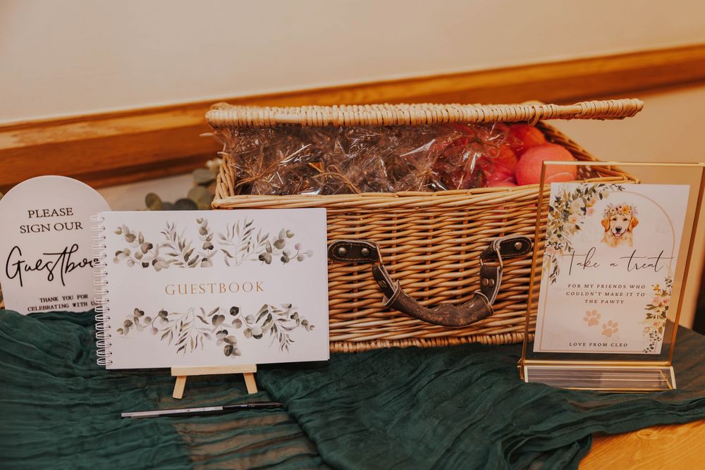 Wedding invitation cards displayed on wooden stands next to a wicker basket on a green velvet tablecloth.