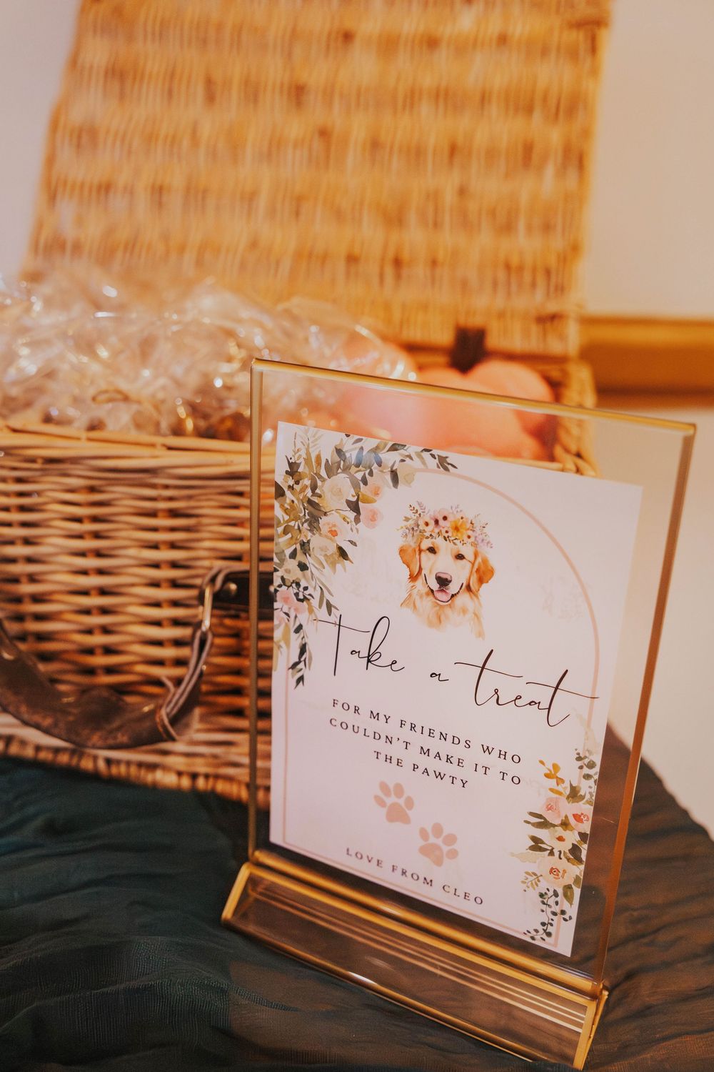 Elegant place cards with floral designs displayed on gold stands against a dark background with a wicker basket visible.