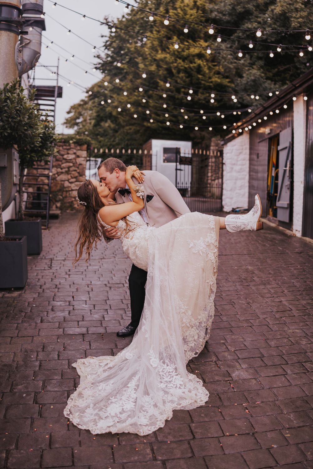 A couple dances romantically on a brick patio under twinkling string lights at dusk.