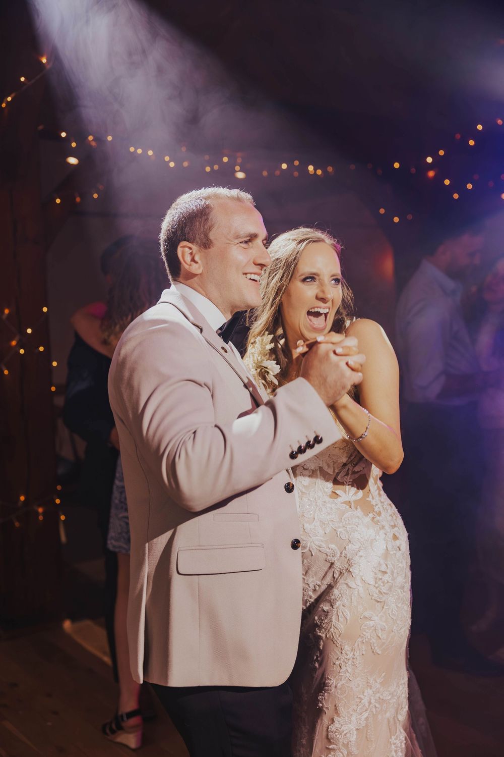 A couple shares a tender moment on the dance floor under glowing lights during their wedding reception.
