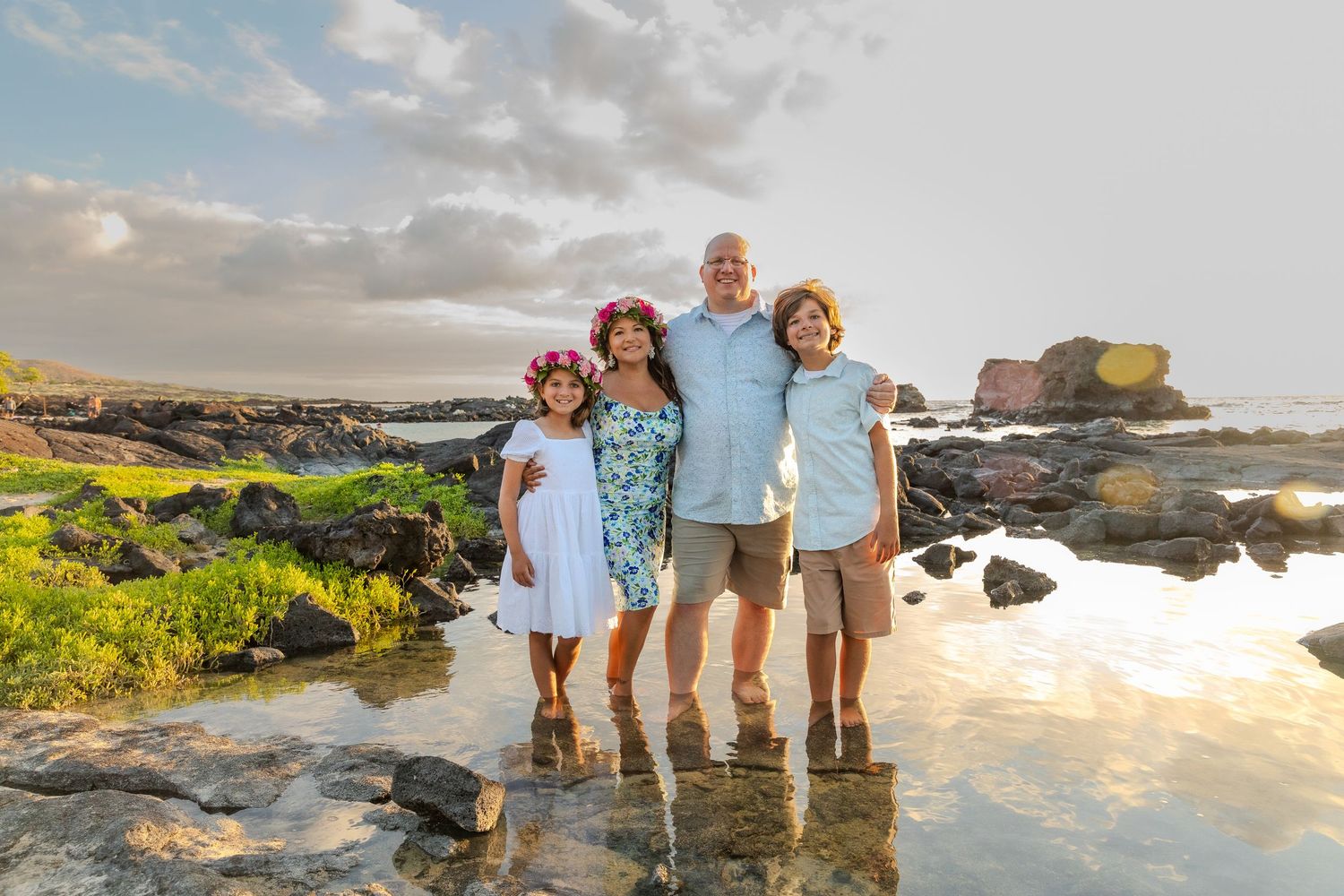 Family group poses casually together under tall palm trees in a tropical setting during golden hour.