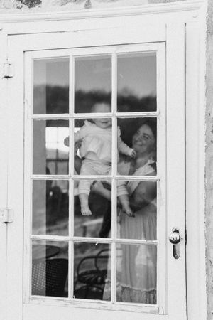 Black and white photograph of people visible through multiple paned windows of a white building.