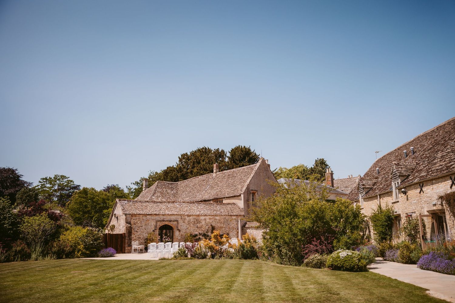 Panoramic view of rustic stone barn buildings and landscaped grounds against a blue sky on a sunny day.