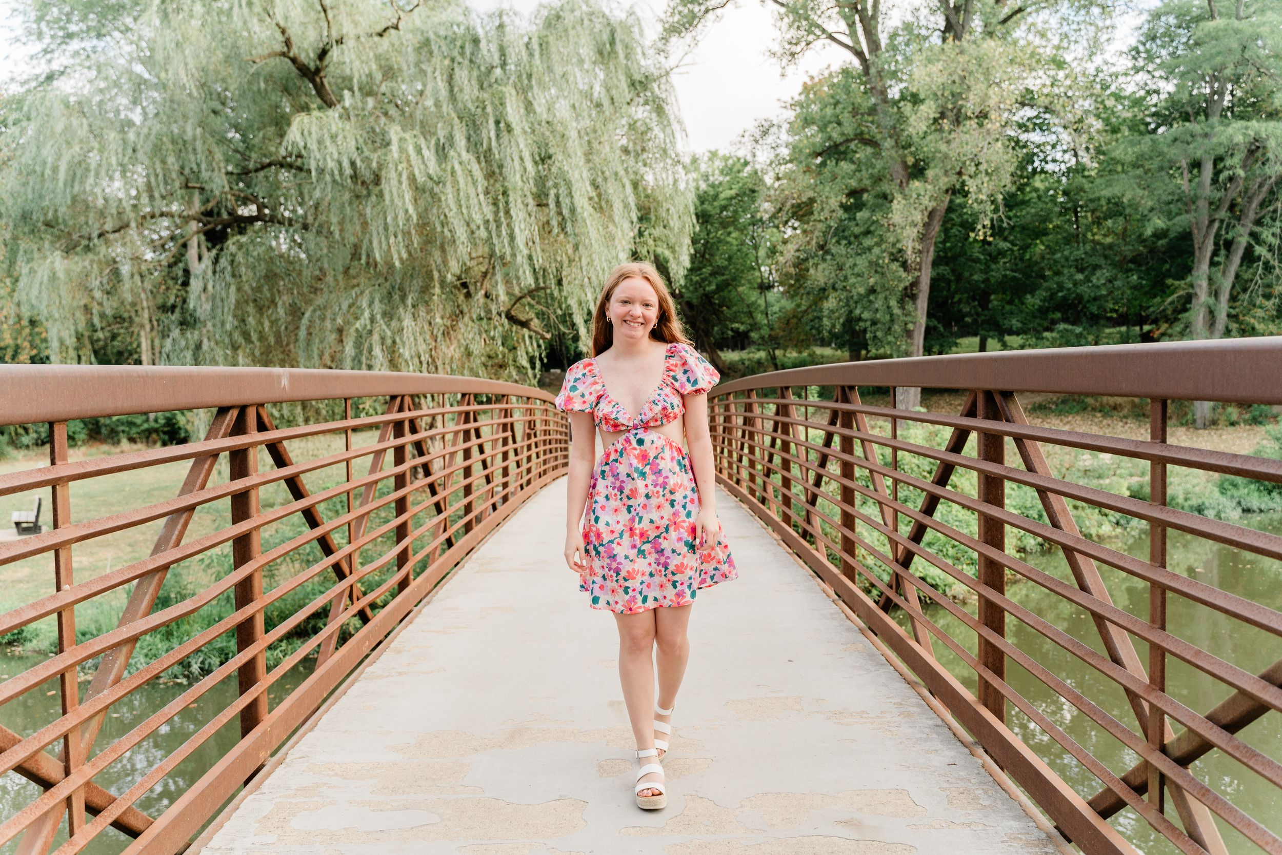 Progressive shots walking across a wooden bridge surrounded by lush green trees and willow branches.
