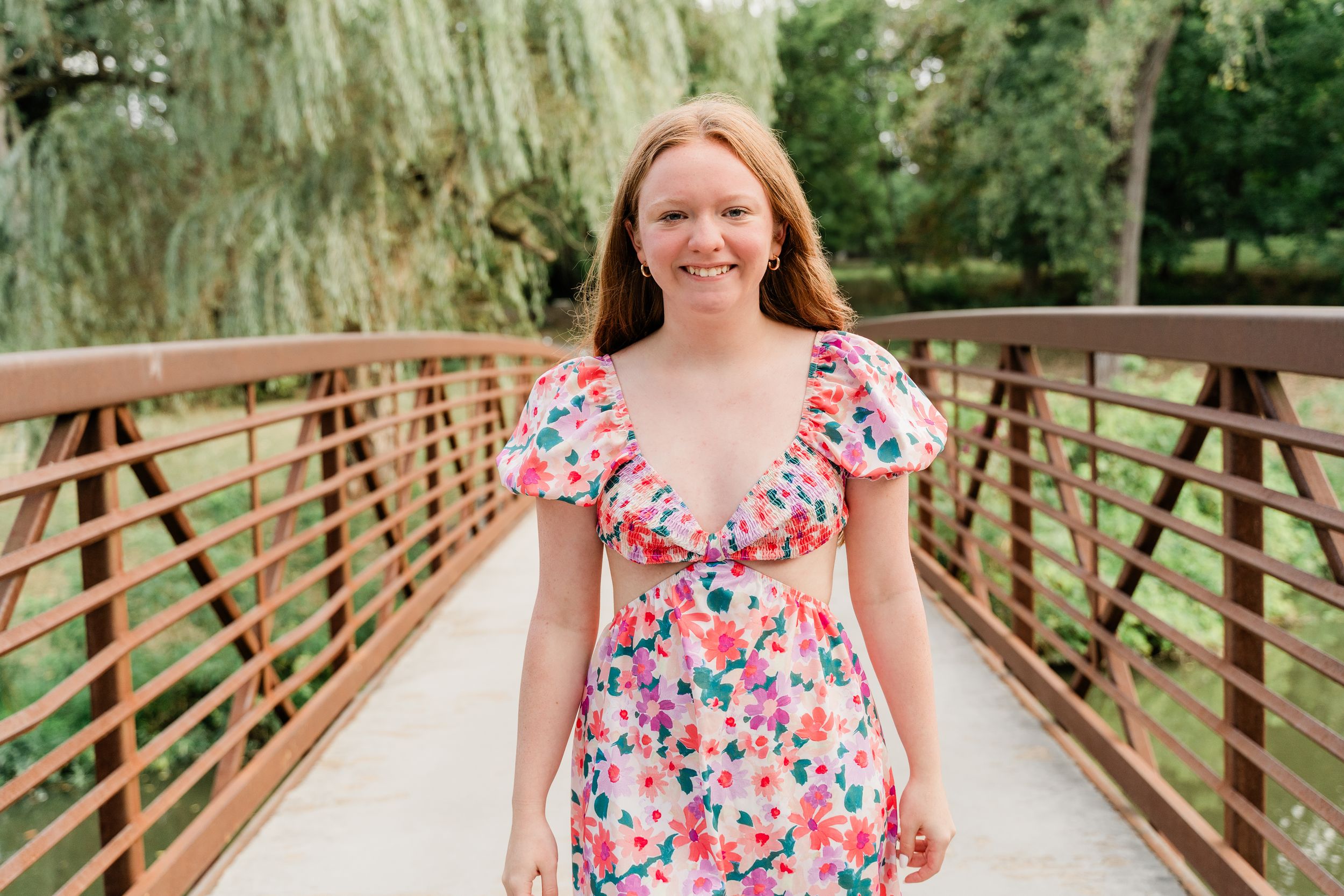 A wooden bridge walkway surrounded by lush willow trees and greenery on a sunny day.
