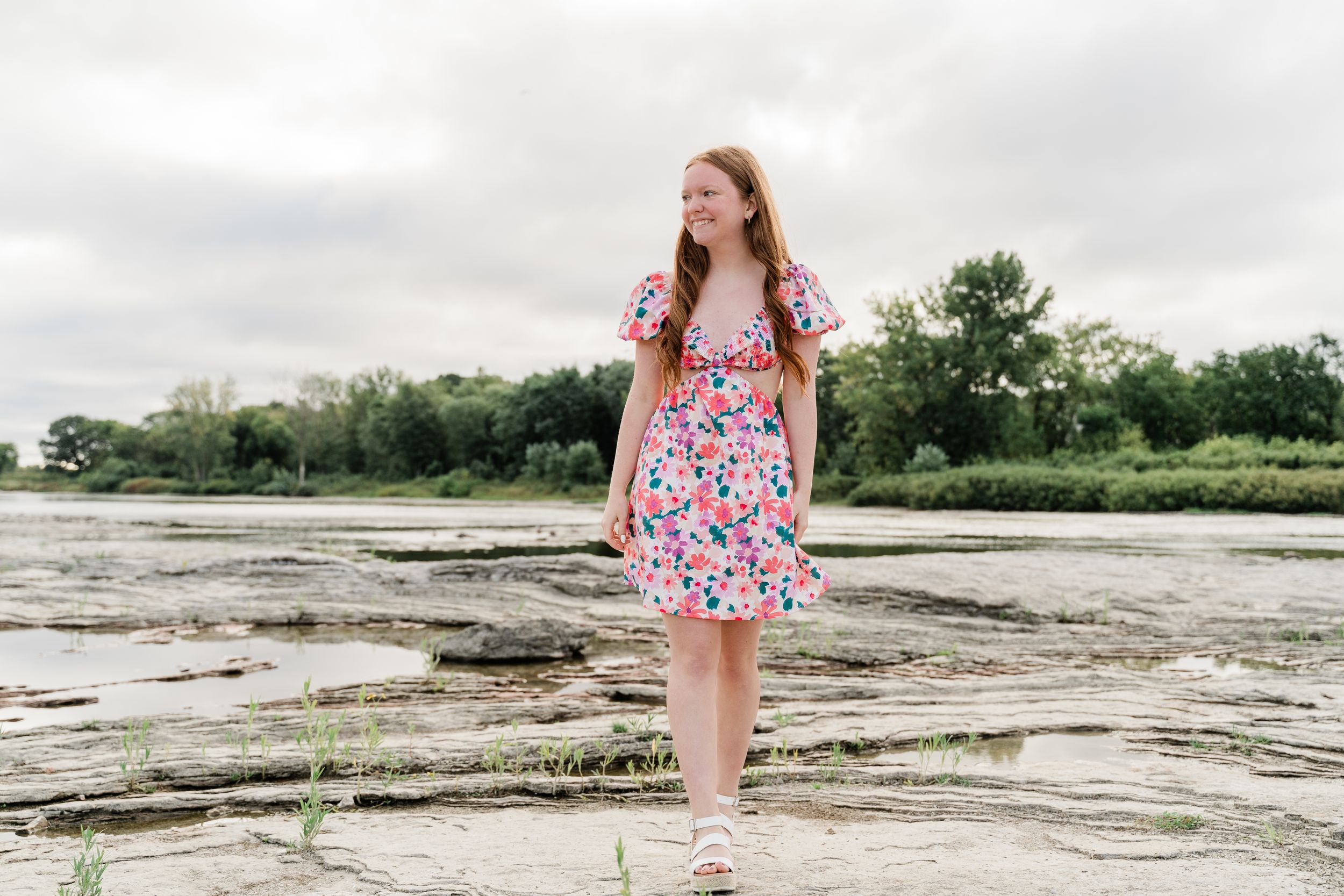 Wide landscape shots on rocky terrain wearing a floral dress against an overcast coastal backdrop.